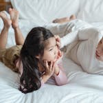 A mother and daughter bonding indoors, lying on a bed and enjoying quality time together.