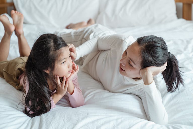 A mother and daughter bonding indoors, lying on a bed and enjoying quality time together.