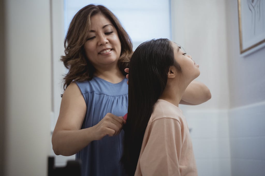 A mother lovingly combs her daughter's hair, symbolizing care and bonding.